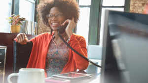 A woman in orange shrug using a traditional landline telephone.