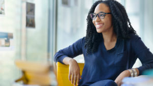 A woman in blue top sitting on yellow chair and smiling