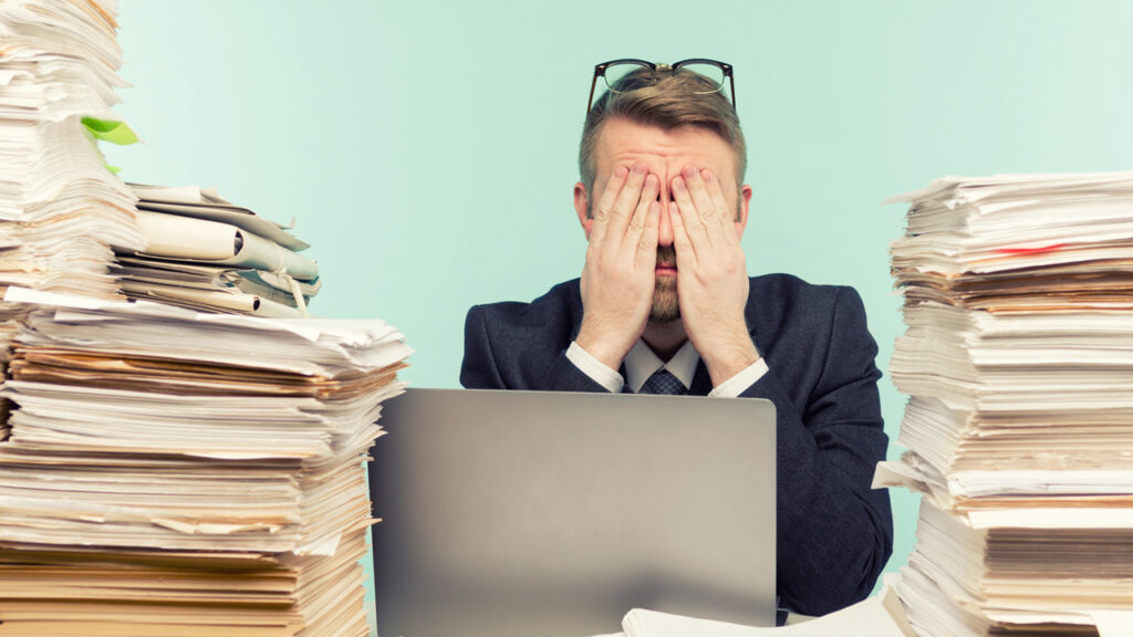 A man sitting stressed between two huge stacks of files