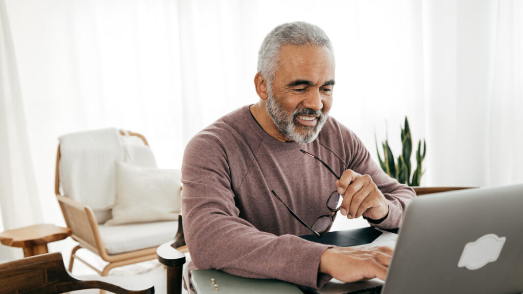 A man holding his spects in his left hand and typing with right hand