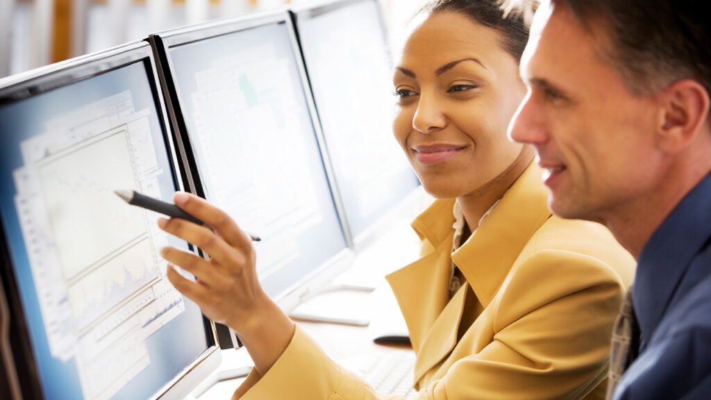 two people in business casual clothing looking at a computer monitor.